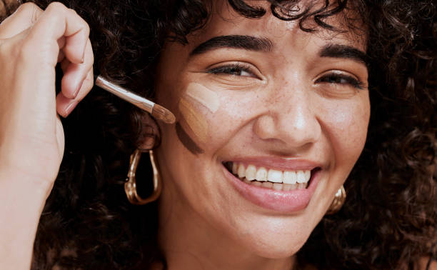 Face, makeup and brush with a woman black model applying foundation to her skin in studio for cosmetics. Portrait, wellness and luxury with an attractive young female using a cosmetic product